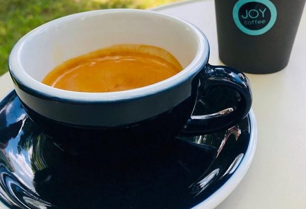 A freshly pulled espresso beside a single-use JOY coffee cup