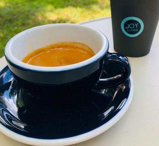 Espresso proaspăt extras, lângă un pahar JOY coffee de unică folosință