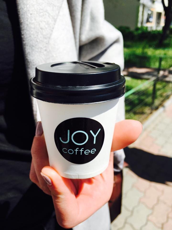 Pahar JOY coffee cu capac, ținut în mână, pe stradă