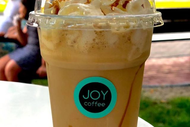 Frappé with whipped cream and caramel in a JOY coffee cup, on the terrace