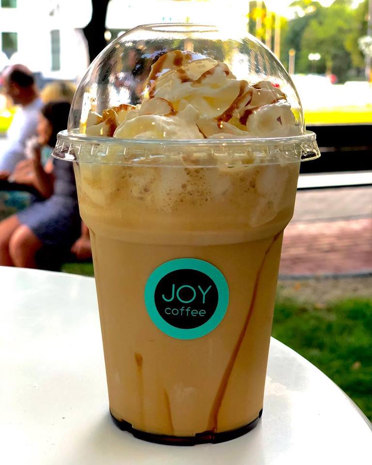 Frappé with whipped cream and caramel in a JOY coffee cup, on the terrace