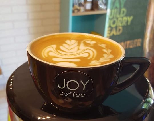 Caffe latte with latte art in a JOY coffee cup, resting on the grinder