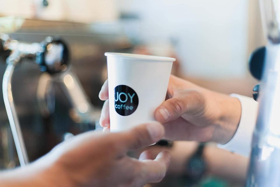 Pahar JOY coffee întins peste tejghea, lângă espressor
